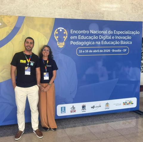 Rodrigo e taciana ao lado do mural azul escrito Encontro Nacional da Especialização em Educação Digital e Inovação Pedagógica na Educação Básica, nos dias 15 e 16 de abril de 2026, em Brasília.
